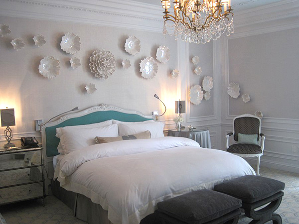 the-bedroom-is-mostly-white-with-a-beautiful-porcelain-flower-installation-and-a-blue-headboard.jpg